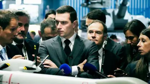 DANIEL DORKO/Hans Lucas/AFP Jordan Bardella (au centre), président du parti Rassemblement National, regarde un modèle de drone militaire Airbus au salon international Eurosatory de l'industrie de la défense et de la sécurité terrestre et aéroterrestre à Villepinte
