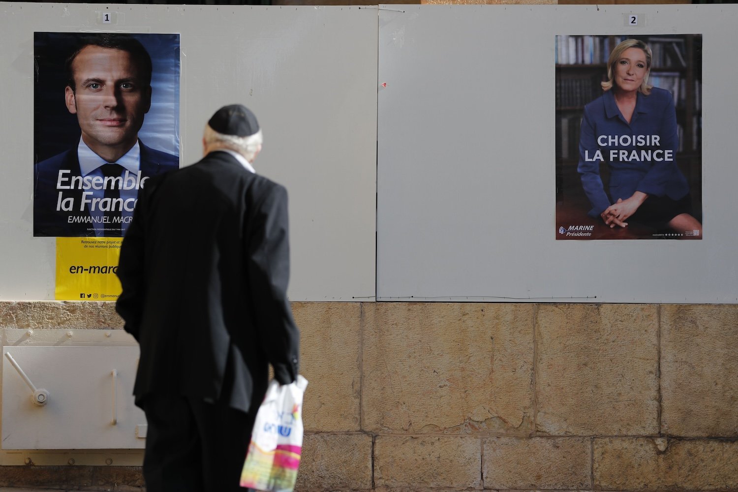 Une personne est vue de dos en train de regarder une affiche de Macron.