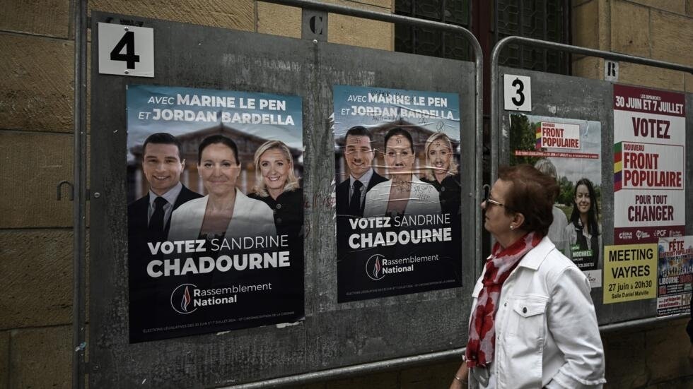 Une femme regarde les affiches électorales de la candidate d'extrême droite française du Rassemblement national (RN) Sandrine Chadournec (C) à Libourne, dans le sud-ouest de la France, le 2 juillet 2024 dans le cadre des élections législatives françaises.